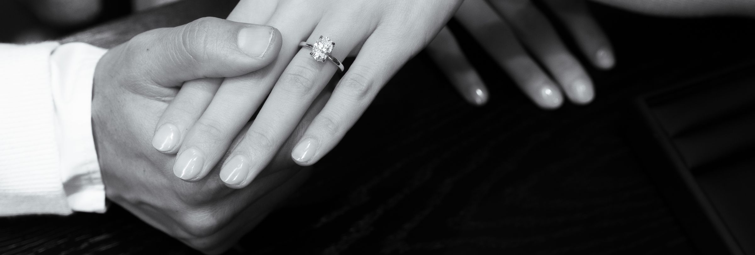 A couple's hands resting together, one wearing a Diamonds Factory display ring